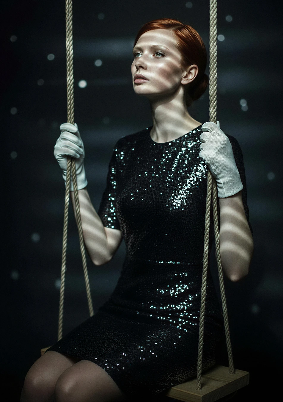 Fashion-editorial met een vrouw in zwarte glitterjurk op een schommel