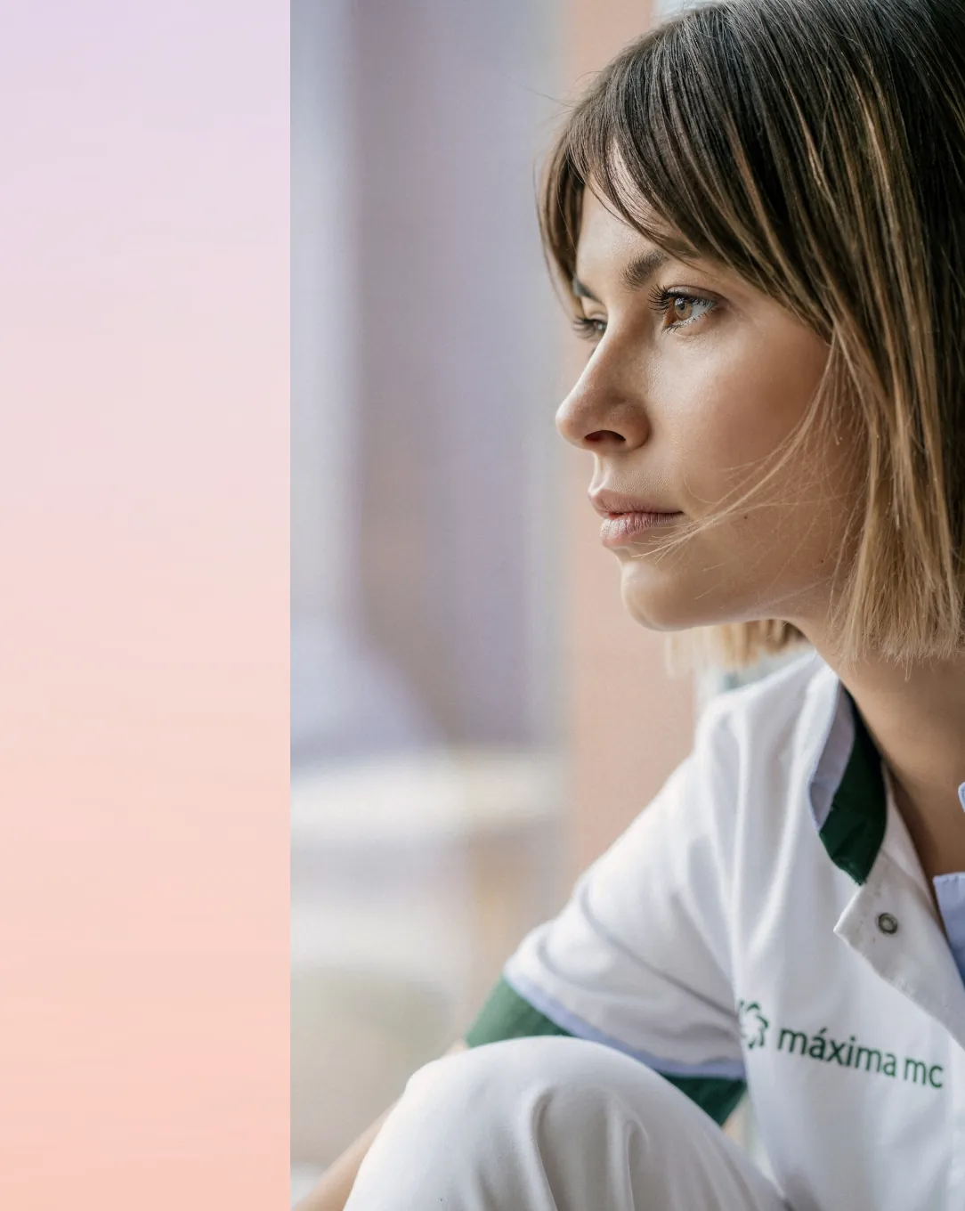 Portret van een zorgmedewerker in wit uniform, starend uit het raam